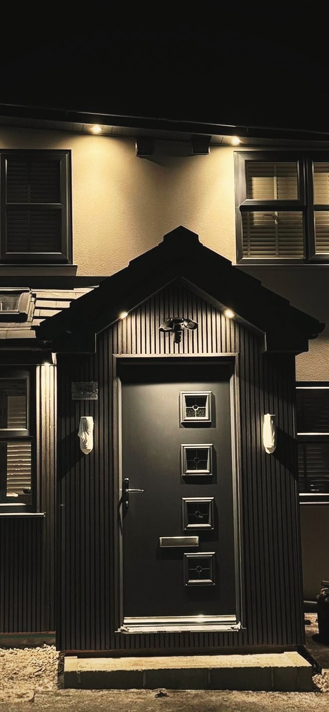 A detached house at dusk with a lit porch, an anthracite composite front door and matching dark window frames
