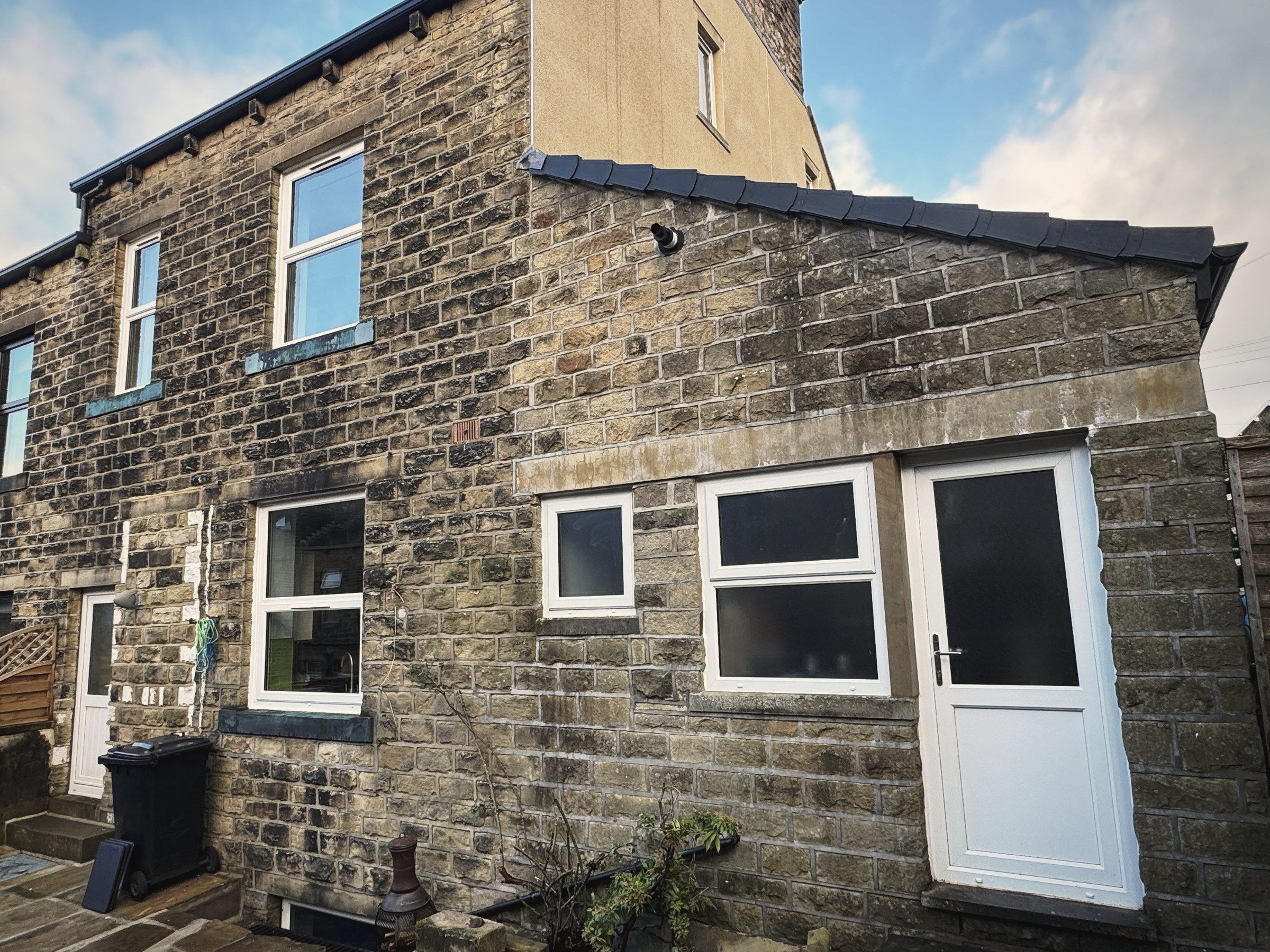 The rear of a stone house with a white uPVC side access door and replacement windows